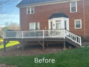 Before photo of an older deck attached to a brick house, featuring a simpler design with white railings and a wooden deck. The yard is grassy with some mulch, and the deck appears smaller and less elaborate compared to the new construction.