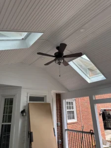 Interior view of a newly built screened porch with a white vinyl beadboard ceiling, featuring two skylights allowing natural light, and a ceiling fan with a modern design.