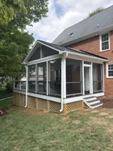 Exterior view of a completed 16'x30' deck and screened porch combo, showcasing a white frame with black screening, a gabled roof, and a wooden deck with black railings.