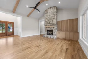 Open great room with floor-to-ceiling stone fireplace, coffered ceilings, built-in cabinetry, and seamless flow to kitchen