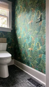 Stylish powder room with natural stone mosaic tile flooring, bold nature-inspired wallpaper, and modern fixtures in Greensboro home remodel by Lakenridge Builders.